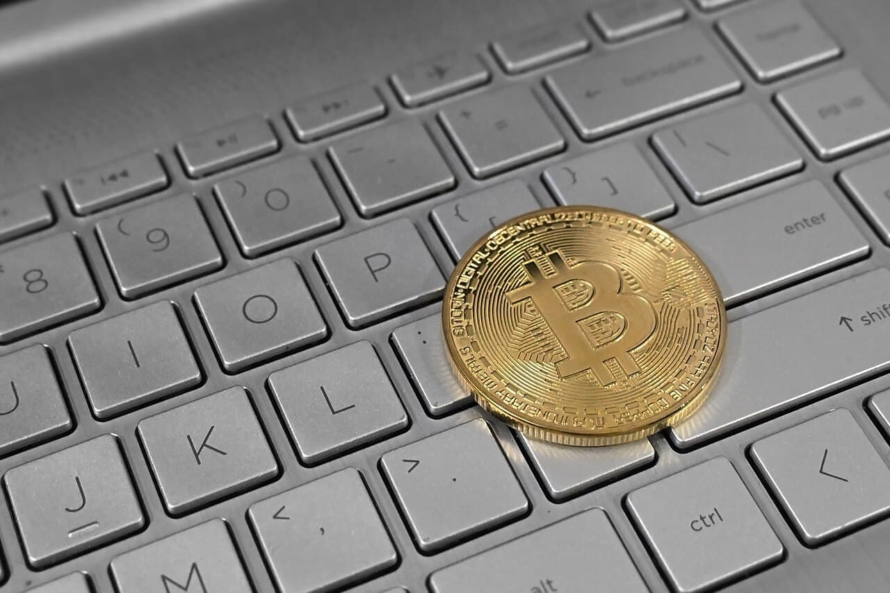 A gold-colored physical Bitcoin token resting on a silver laptop keyboard.