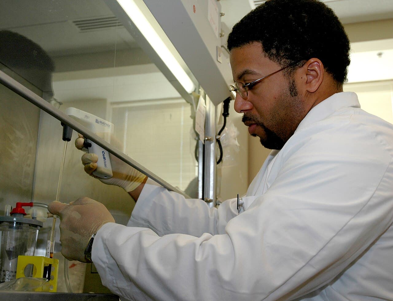 A researcher draws a sample with a pipette under a laboratory fume hood.