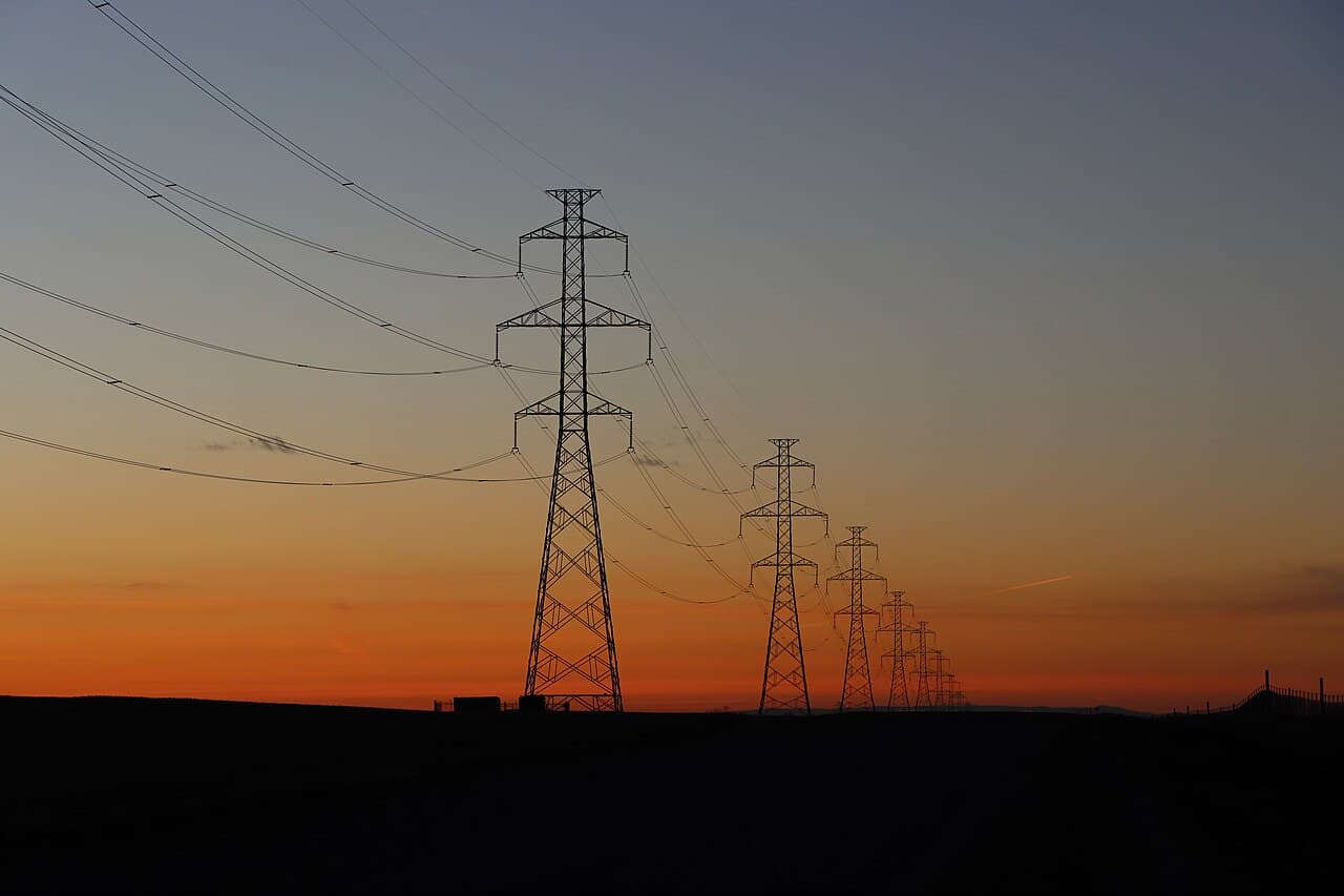 High-voltage transmission towers silhouetted against the sky at sunset.