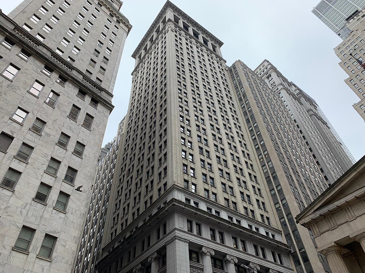 Looking up at 14 Wall Street and neighboring office towers in Lower Manhattan's Financial District on a cloudy day.