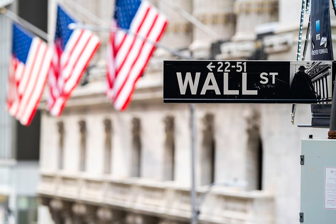 A Wall Street street sign in front of the flag-hung facade of the New York Stock Exchange.